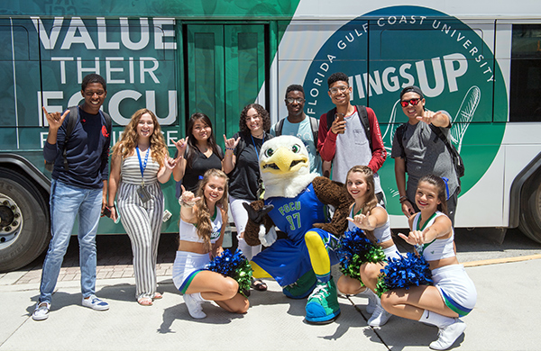 Students and Azul mascot with wings-up hand shape in front of FGCU themed bus