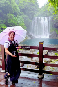 Alora, female mentor  standing in front of water fall with pink umbrella