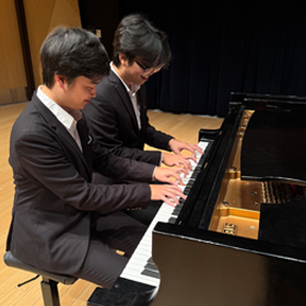 2 studdents in concert dress playing on a piano