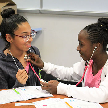 Picture of a young girl using a stethoscope on another young girl.