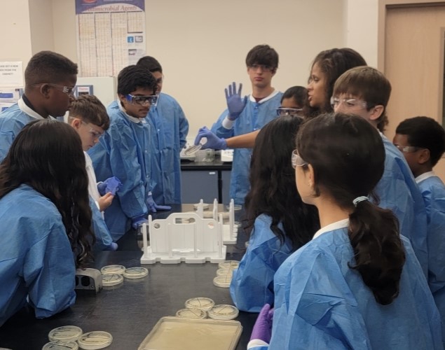 Middle school students gathered around a table wearing labcoats