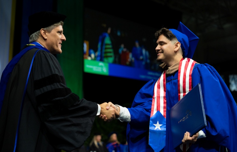 Dean Chris Westley shakes hands with a graduating student from the Lutgert College of Business on stage during the Spring 2026 commencement ceremony.