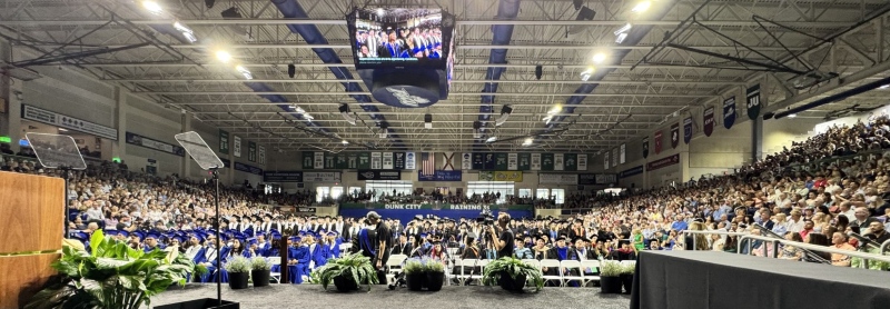 Graduates are seated across a full arena floor at Alico Arena during Florida Gulf Coast University’s Spring 2026 first commencement ceremony.