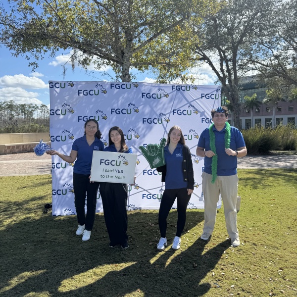 students posing in front of an FGCU backdrop on the Library Lawn