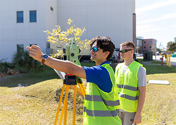 Two students in yellow vests conduct field surveying