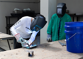 A student welds two metal pieces together while a professor watches