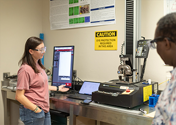 A student wearing goggles uses a machine to test how much different materials can bend