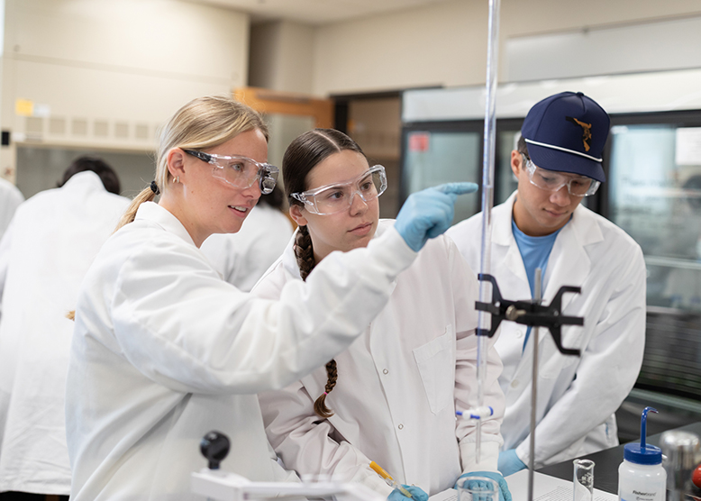 Two students using wearing lab coats look closely at a test tube