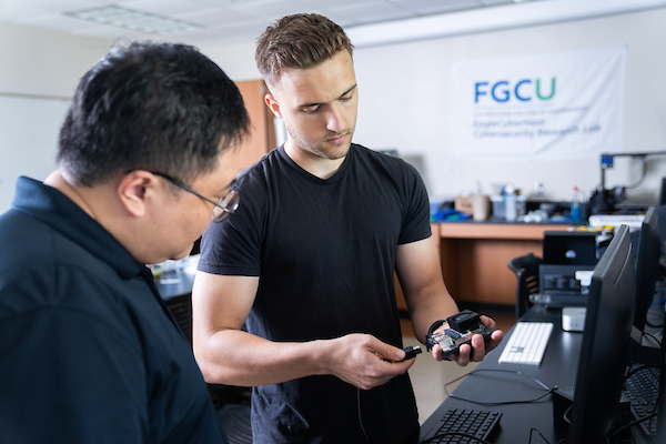 A student and professor look at a piece of cybersecurity equipment in a lab space