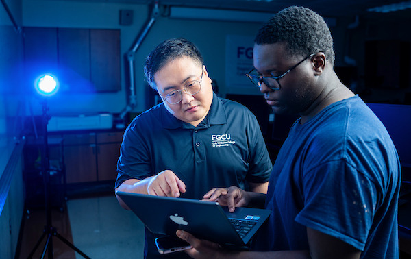 A student and professor look at a laptop together in a lab space with blue lighting