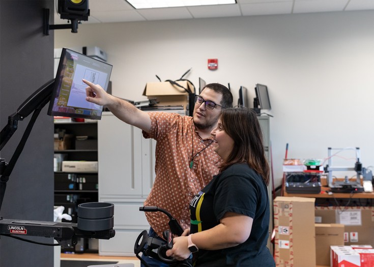 A lab manager shows a student how to use the VR welding tools