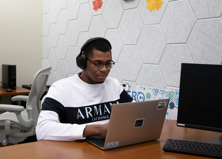 A student wearing headphones works on a laptop