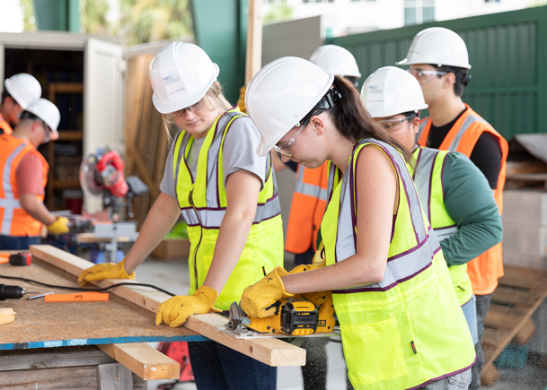 A construction management student saws through a 2x4 board