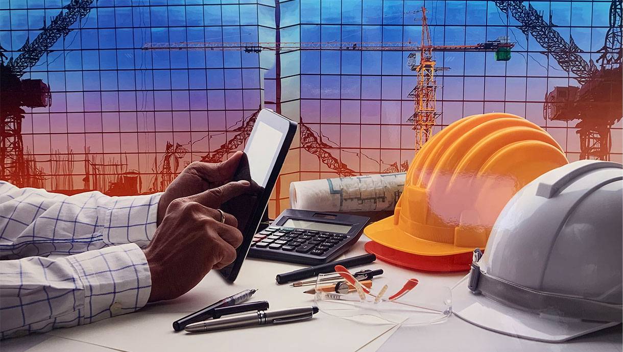 Hands hold a calculator next to a construction hat.