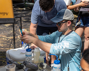 A student in a hat tests water in a container