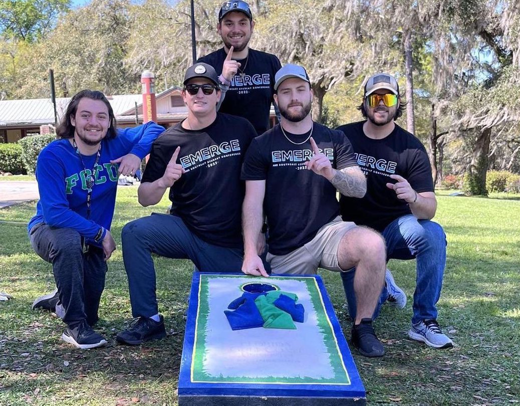 Group of students posing with a cornhole board