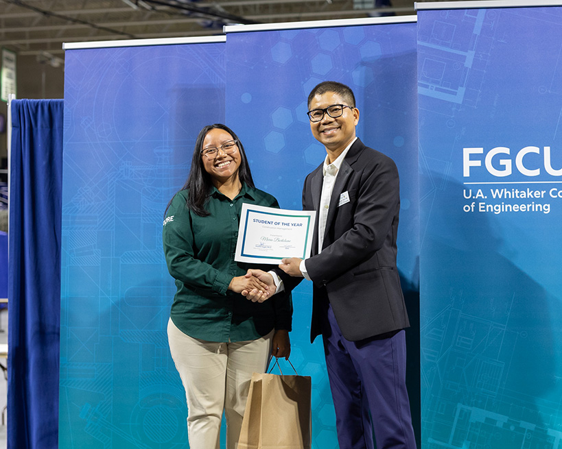 A woman in a green button down holding a certificate and shaking the hand of a man in a suit