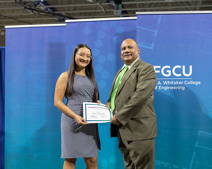 A woman in a patterned dress poses with a certificate next to a man in a suit