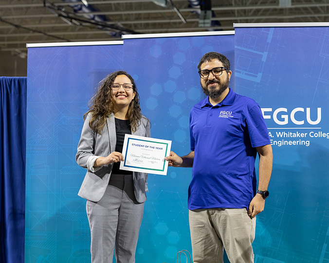 A woman in a gray blazer holds a certificate next to a man in a blue polo