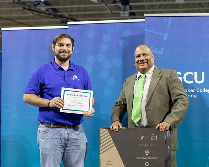 A man in a blue polo holds a certificate next to a man in a suit