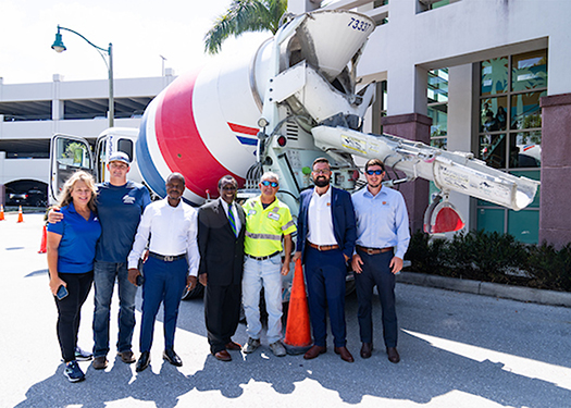 A group of people stands in front of a concrete mixing truck