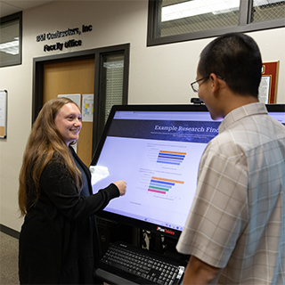 A graduate student talks to her mentor while looking at a big screen