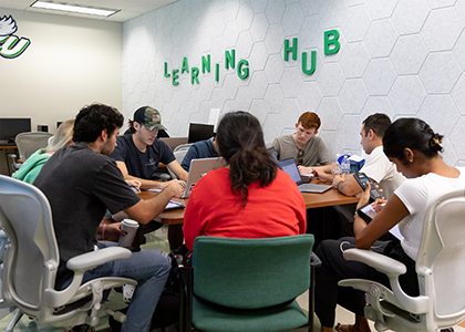 A group of students studies for an exam together with the words "Learning Hub" decorating the wall behind them.