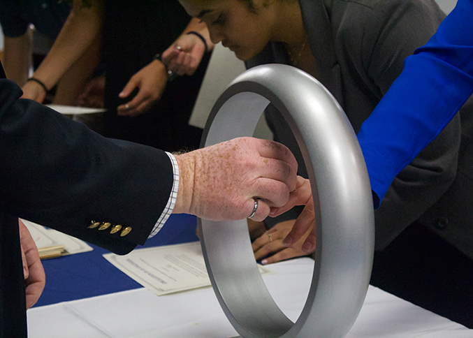 A hand places a silver ring on the hand of an inductee through a large silver circle.