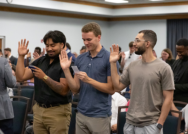 Three inductees hold their hands up while reading the oath
