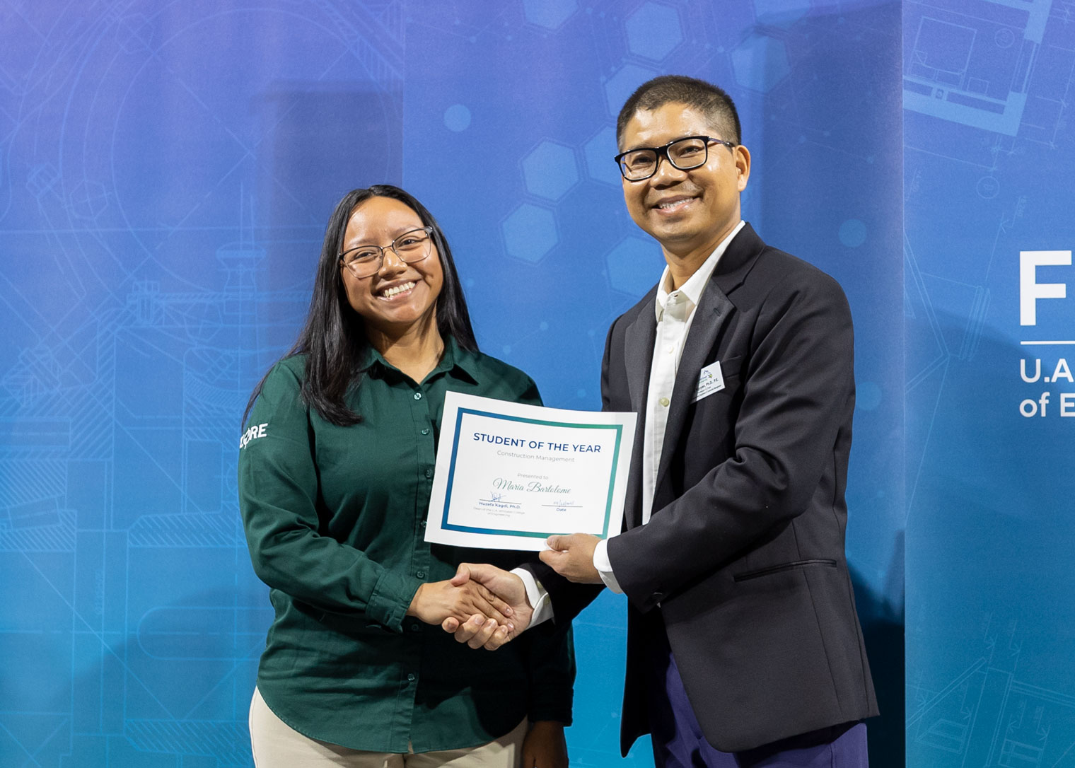 A student holds an award while standing next to a professor