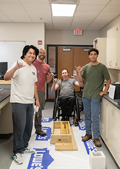 Four students do the wings up hand signal near a wooden mold