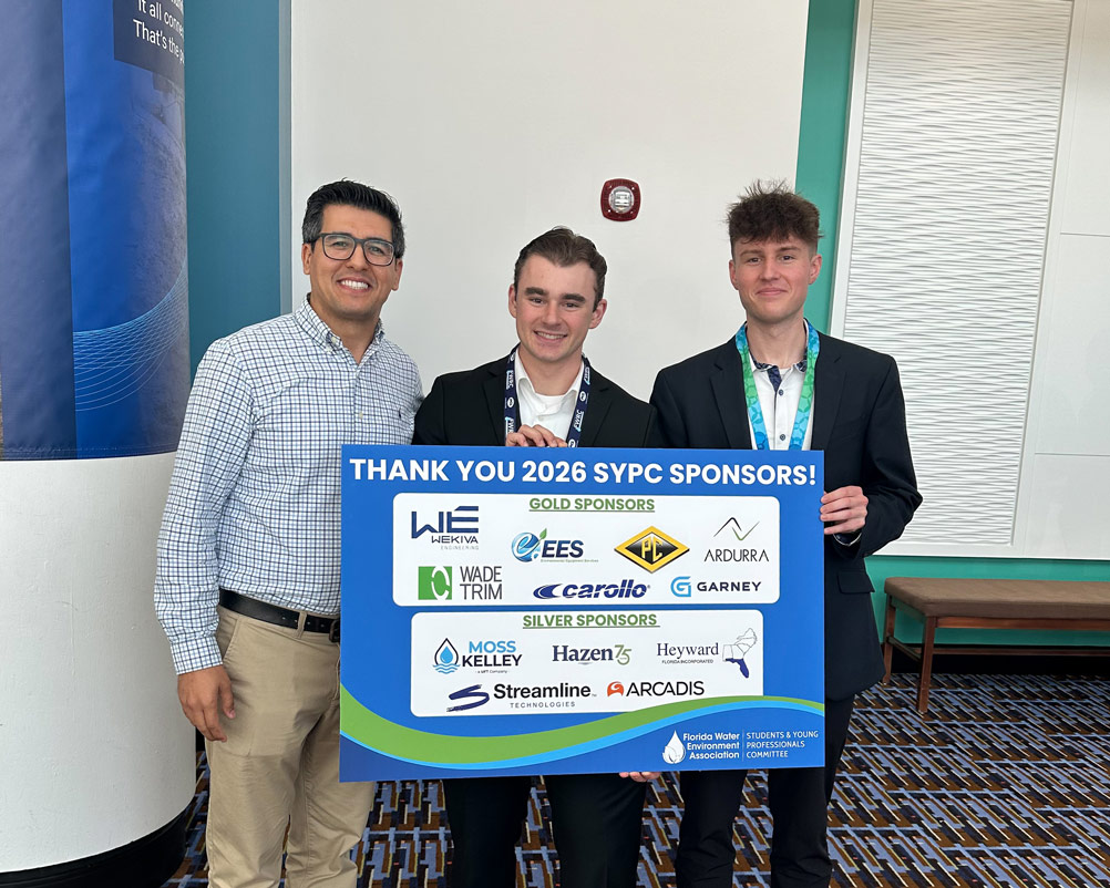 Carter and Zach pose with Dr. Osman Karatum and a sign thanking the sponsors of the FWEA competition