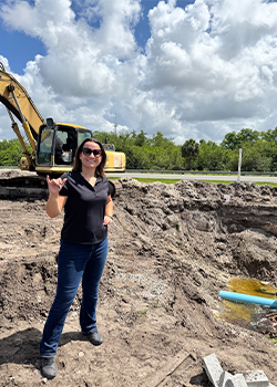 Hannah at her internship A student stands in front of a crane, doing the "wings-up" hand gesture