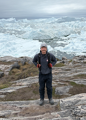 A student wearing a backpack and smiling stands in front of a field of ice.