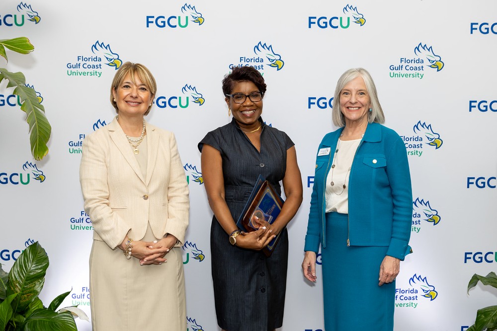 Three women stand in front of a Florida Gulf Coast University backdrop at the 2026 Celebration of Excellence Award Ceremony. The woman in the center holds a plaque recognizing the Senior Faculty Teaching Excellence Award, while the two women beside her stand smiling.
