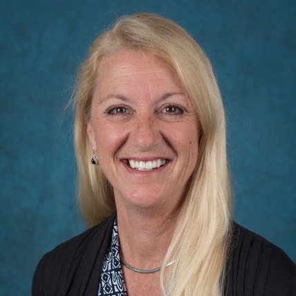 Headshot of Beverly Brown. She has long blonde hair and is wearing a blue and white blouse with a black cardigan. 