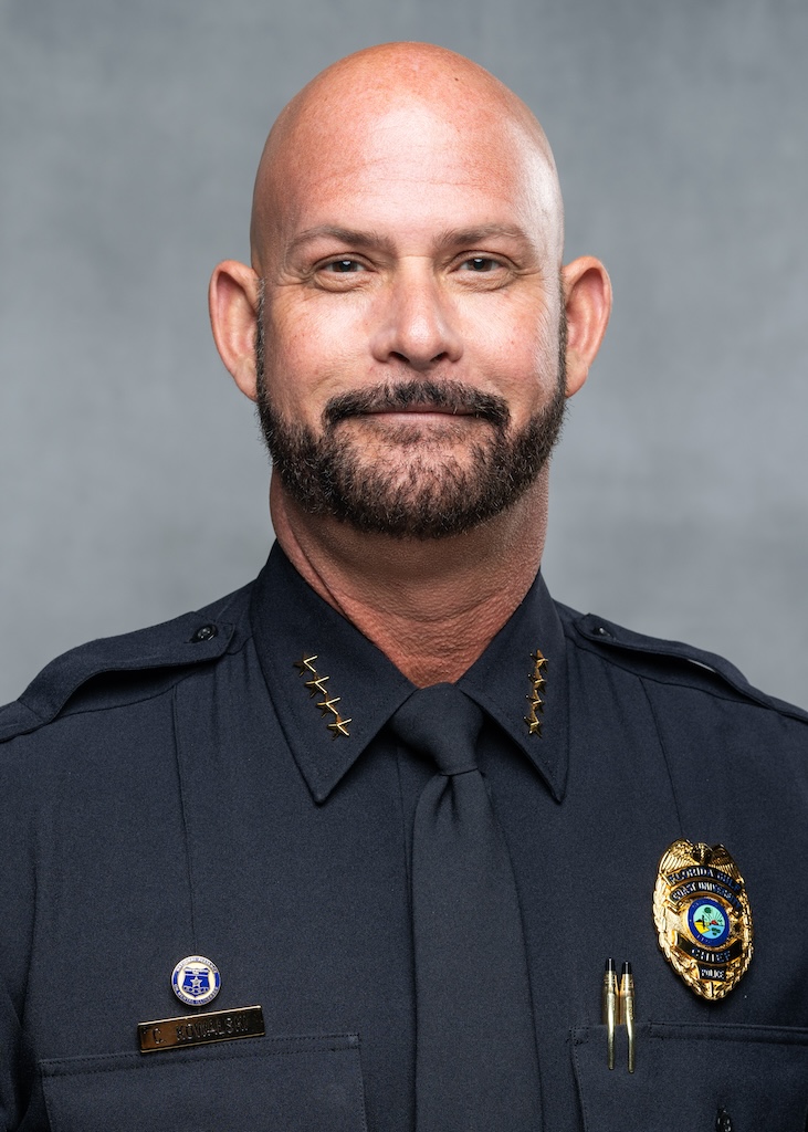 Headshot of FGCU’s Chief of Police Craig W. Kowalski. He is wearing a dark blue police uniform and tie. Both right and left collars of this shirt have 4 gold stars pinned on each side. A police pin and his name tag are pinned to the right side of his uniform. On the left side is his badge and two pens sticking out from a breast pocket.  