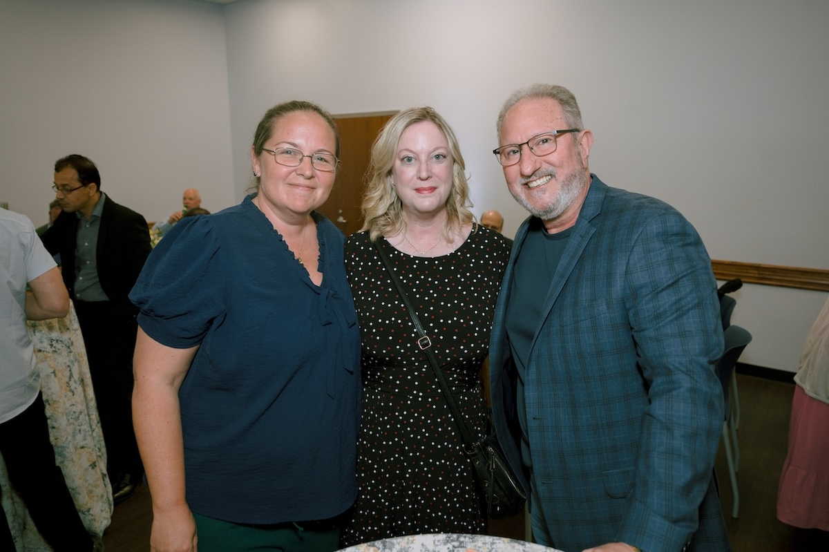  Three FGCU employees gather for a photo at the Celebration of Excellence reception. The person on the left has her hair pulled back in a ponytail and is wearing glasses and a dark teal blouse. The person in the middle has short blond hair and is wearing a black blouse with white and red polka dots. The person on the right is wearing glasses and a teal t-shirt underneath a light teal blazer. 