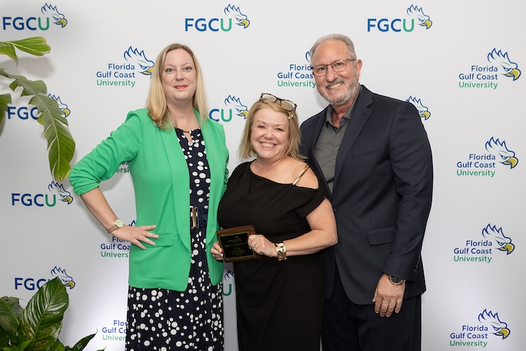 Three FGCU employes pose for a photo in front of a white FGCU step-and-repeat.