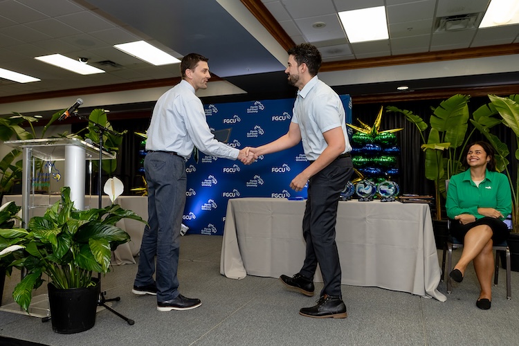An FGCU employee walks up to the stage to receive his award and shakes the hand of the award presenter.