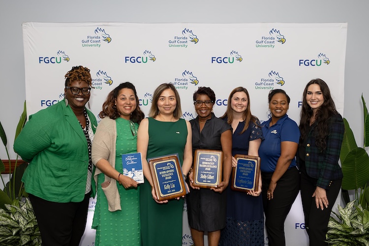 Seven FGCU employees dressed in green and blue clothing pose for a photo in front of a white FGCU step-and-repeat. The four women in the middle are holding blue plaque awards.