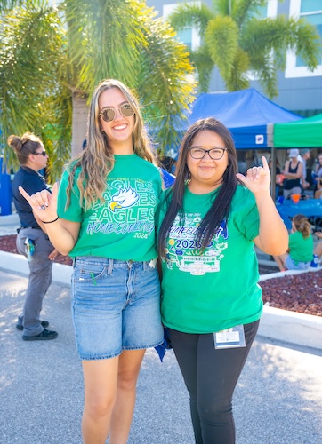 Two FGCU employes dressed in green FGCU t-shirts give the Wings Up sign.