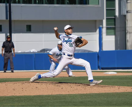 FGCU baseball player, dressed in a white uniform with the word “Eagles” and the number 32 displayed on his chest in blue and green colors, is throwing a pitch while on a baseball field. His teammate, wearing the same uniform, is in the background. 