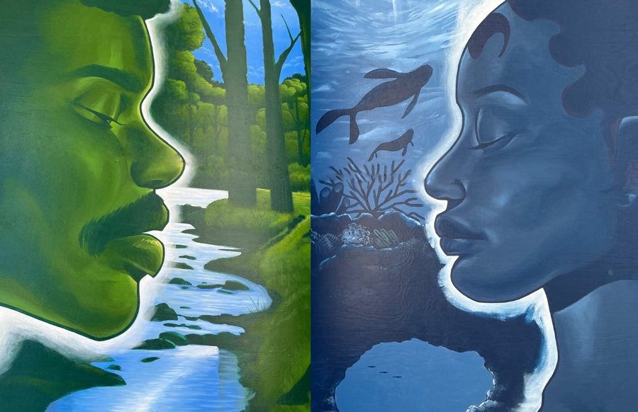 Painting- Paul Firmin, “Heart & Soul,” 2024, Acrylic on four panels. The left side of the painting shows the face of a man painted in green with a blue river, green trees and a portion of the sky in the background. The right side of the painting shows a women pained in blue. In the background you can see a view of the ocean, and coral reef and sea animals shown in a darker shade of blue.   