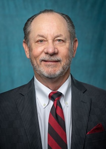 Headshot of Joseph Groch. He is wearing a white button-down shirt, a red and black tie, and a black blazer. 