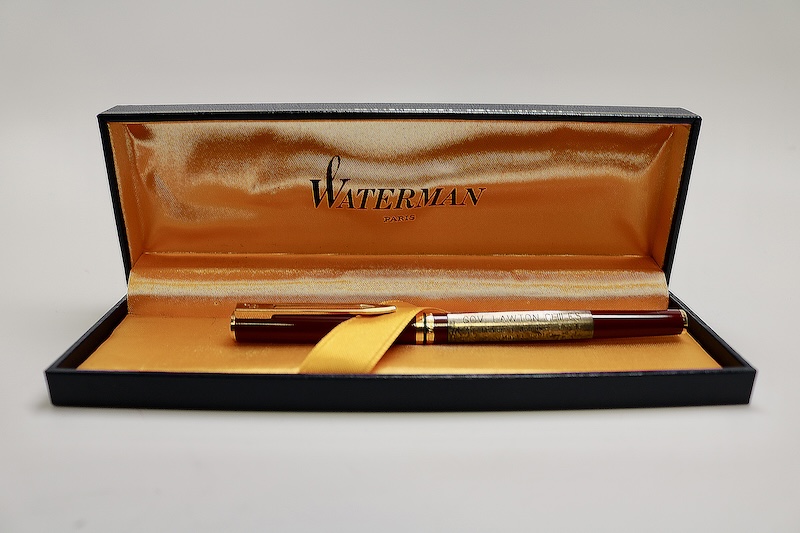 An open Waterman-branded pen case with an orange interior lining, displaying a pen secured by a ribbon inside the box.
