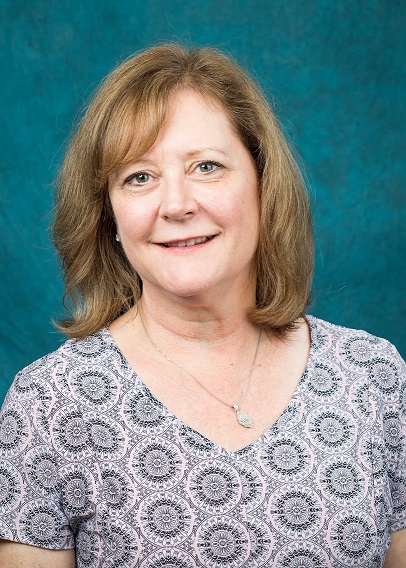 Headshot of Lori Zallie. She has short blond hair and is wearing a necklace and a light grey blouse with a circle pattern.