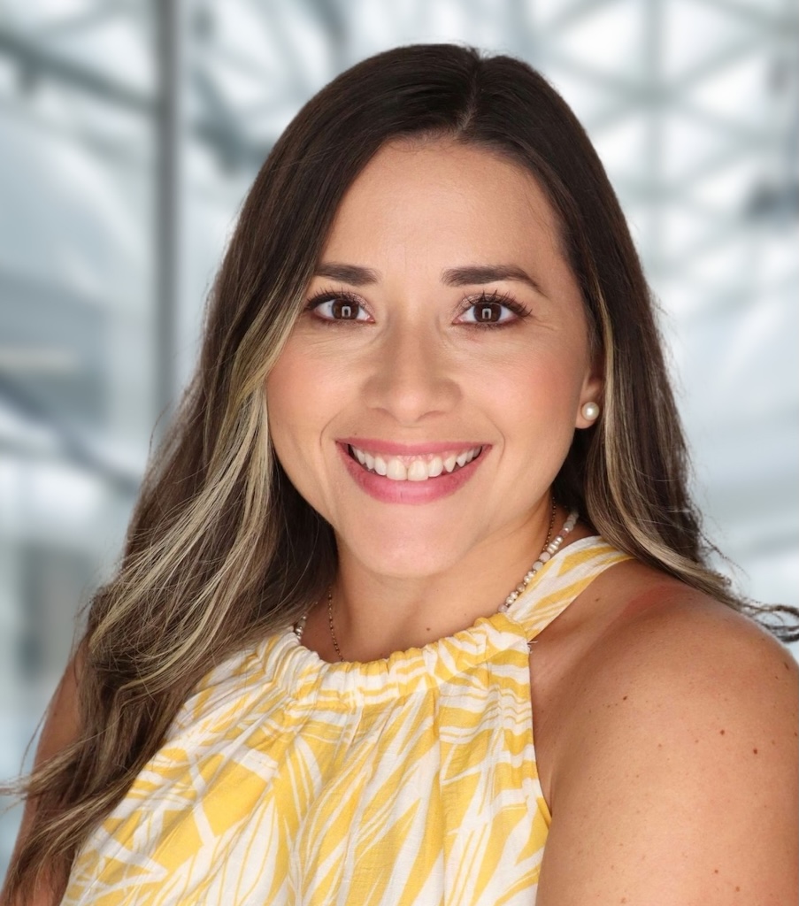 Headshot of Maria Sotomayor. She has long, dark hair and is wearing a sleeveless yellow and white patterned top.