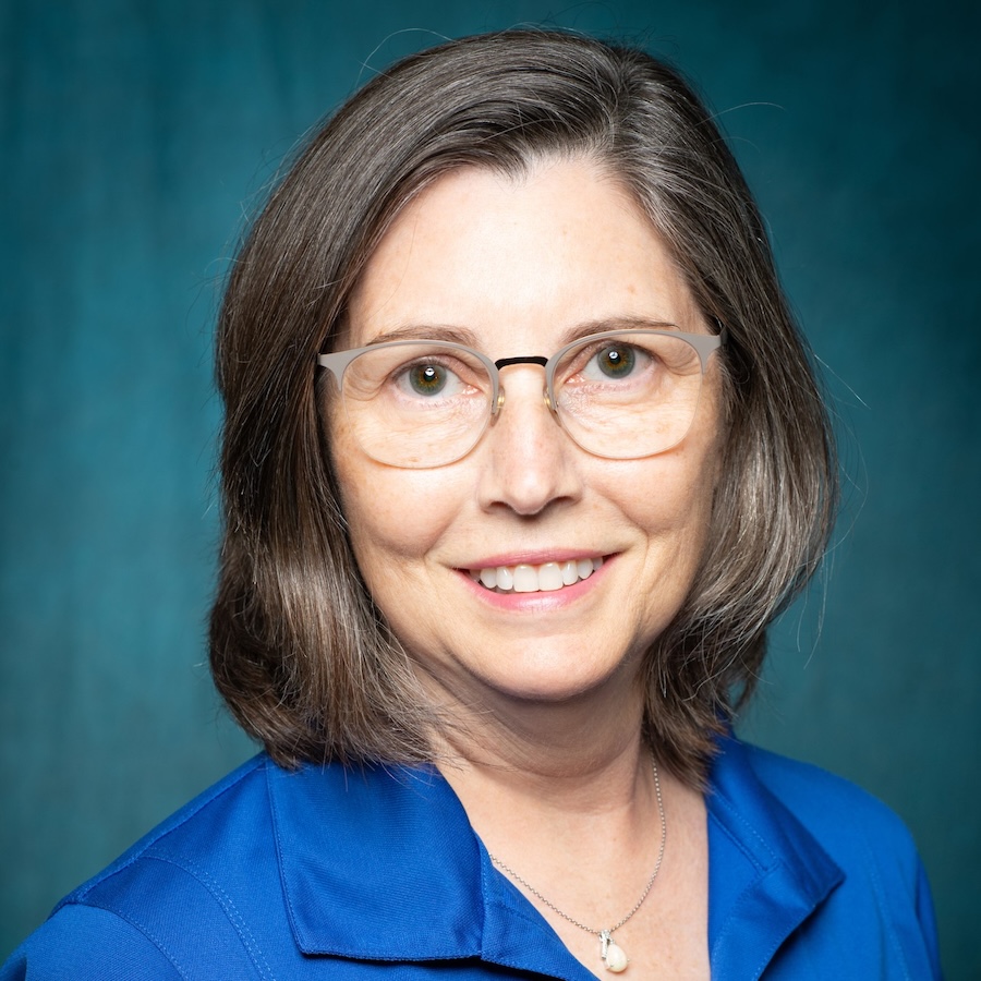 Headshot of Nadia Payne. She has short hair and is wearing a necklace, glasses and a blue polo shirt.  