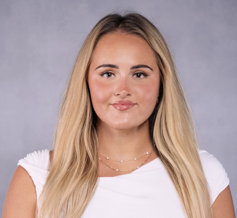 Photo of Sara Niepelova with long, straight blonde hair, wearing a white top. She is facing the camera with a neutral expression. The background is plain gray, providing a clean and professional setting.